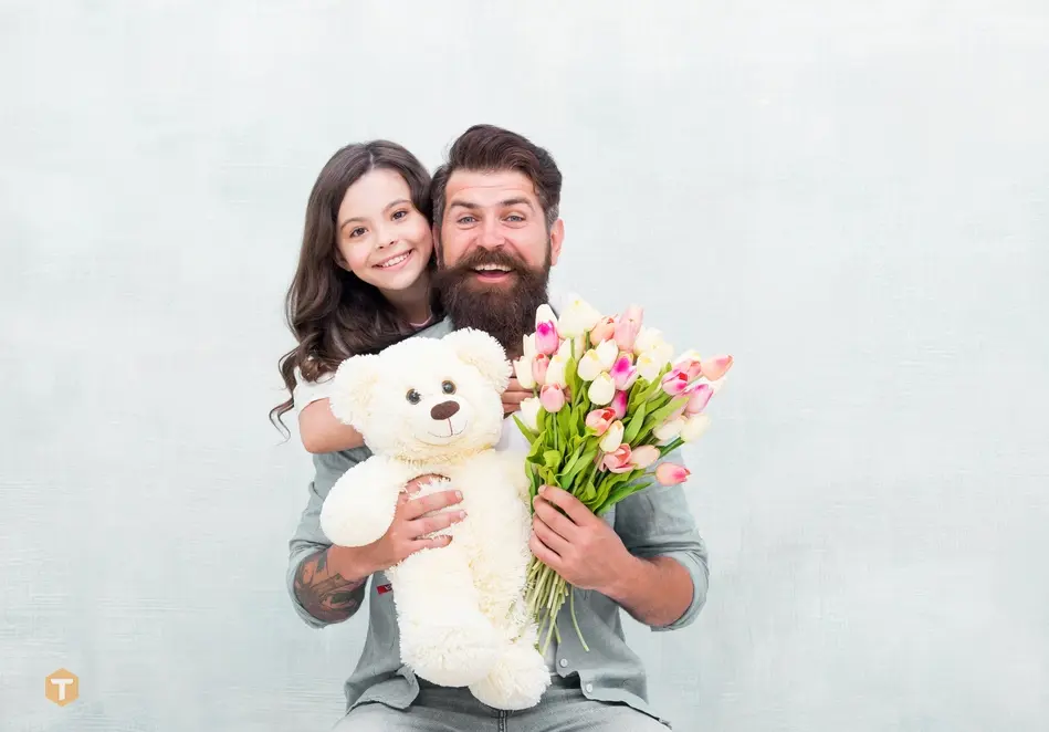 یک پدر و دختر خندان با خرس عروسکی سفید و دسته گل